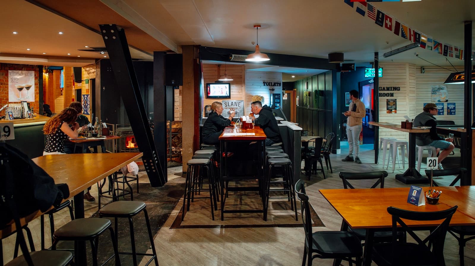 Inside Biddy Kate's Cafe Bar, Blenheim — guests at tables with the fire going and flags overhead